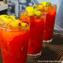 Three bloody Mary's on the bar with olives and lemons across the top