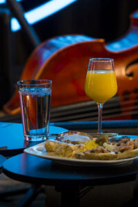 A plate of food, glass of water, and wine glass with orange juice in front of a bass resting on its side